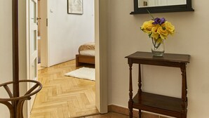 Un pasillo con suelo de madera, un perchero, un espejo y un florero con flores sobre una mesita.