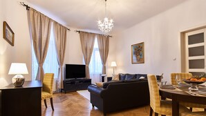 Una sala de estar con sofá, sillas, una mesa de comedor, televisor y candelabro.