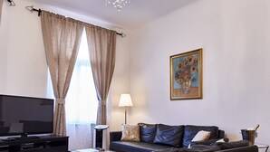 Una sala de estar moderna con un sofá negro, un televisor de pantalla plana, una araña y un cuadro en la pared.