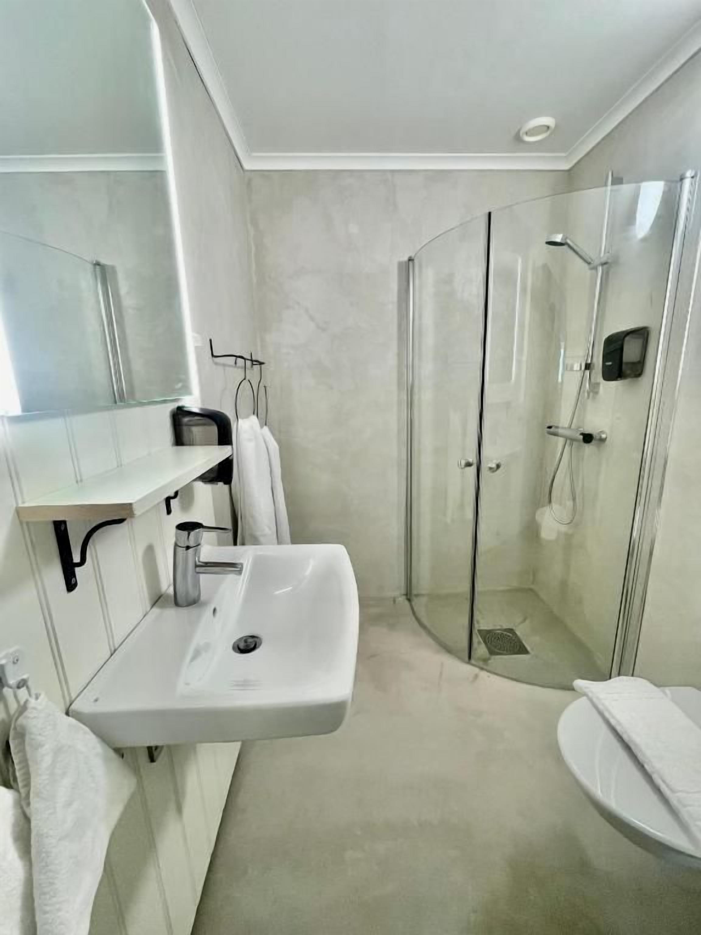 Casa de banho moderna com cabine de duche em vidro, lavatório branco e espelho.