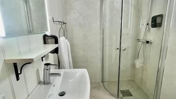 Casa de banho moderna com cabine de duche em vidro, lavatório branco e espelho.