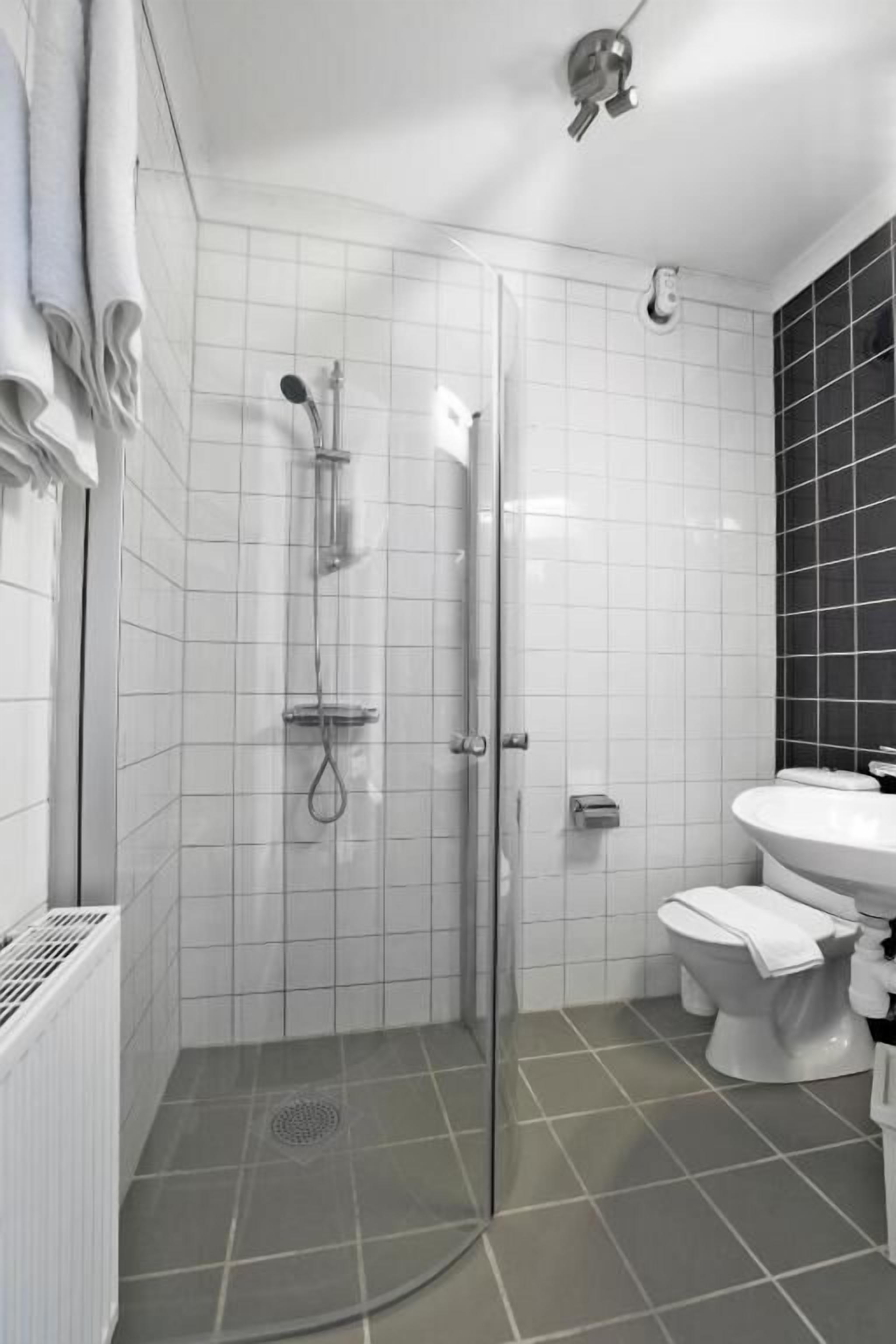 A modern bathroom with a glass-enclosed shower, white tiles, a white sink, and a toilet.