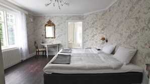 A bedroom with a large bed, a small desk, a chair, and a mirror. - Ardrebo B&B (Ljugarn)