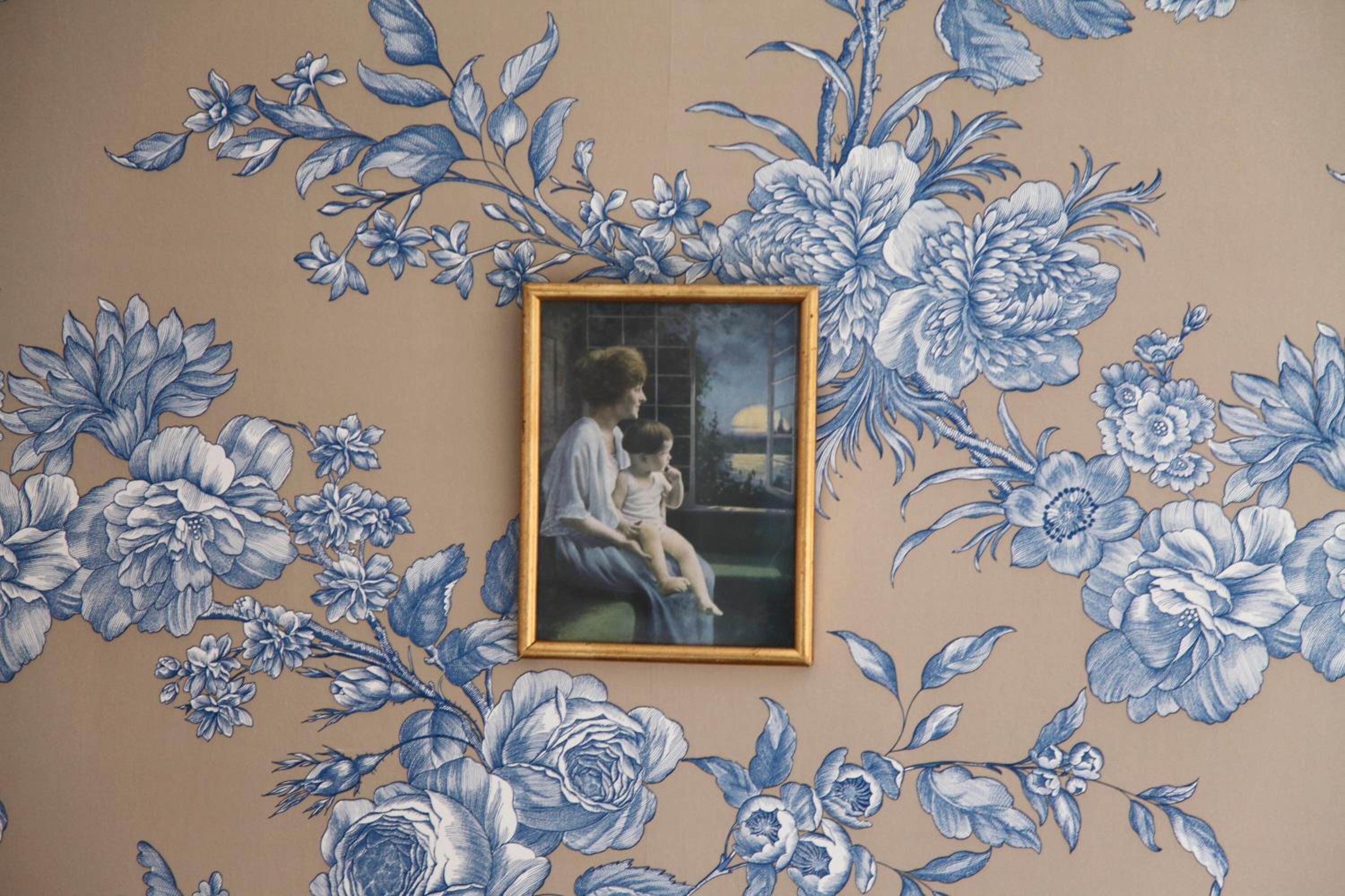A wall with a floral pattern and a framed painting of a woman and child.