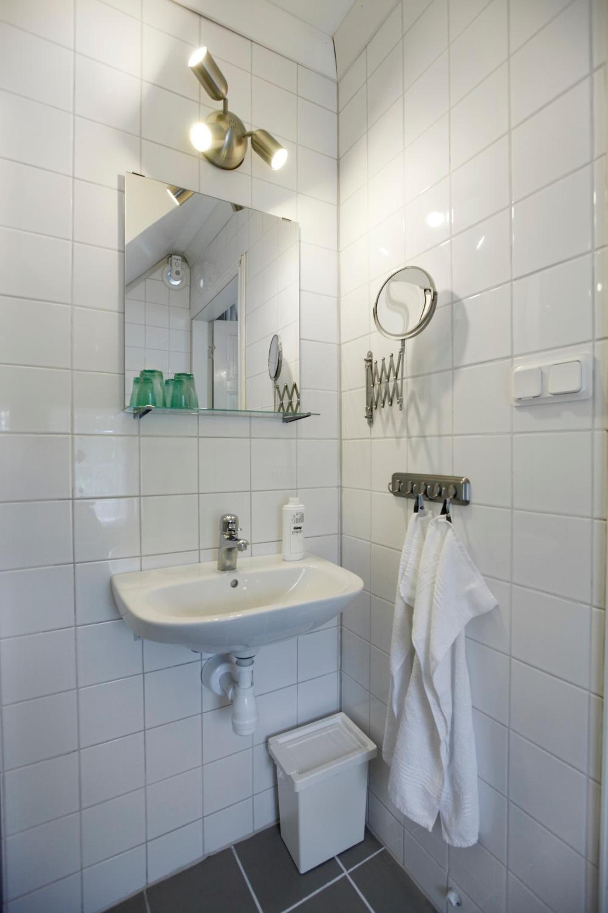 Un baño con lavabo blanco, espejo y perchero para toallas.