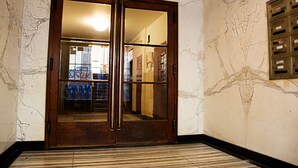 A wooden double door with glass panels, leading to a hallway with a tiled floor and a marble wall. - Wenceslas Square Apartment (Prague)