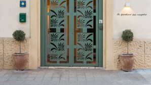 A building entrance with a decorative green door, a small sign above the door, and two potted plants on either side. - Al Giardino Del Nespolo (Polignano a Mare)