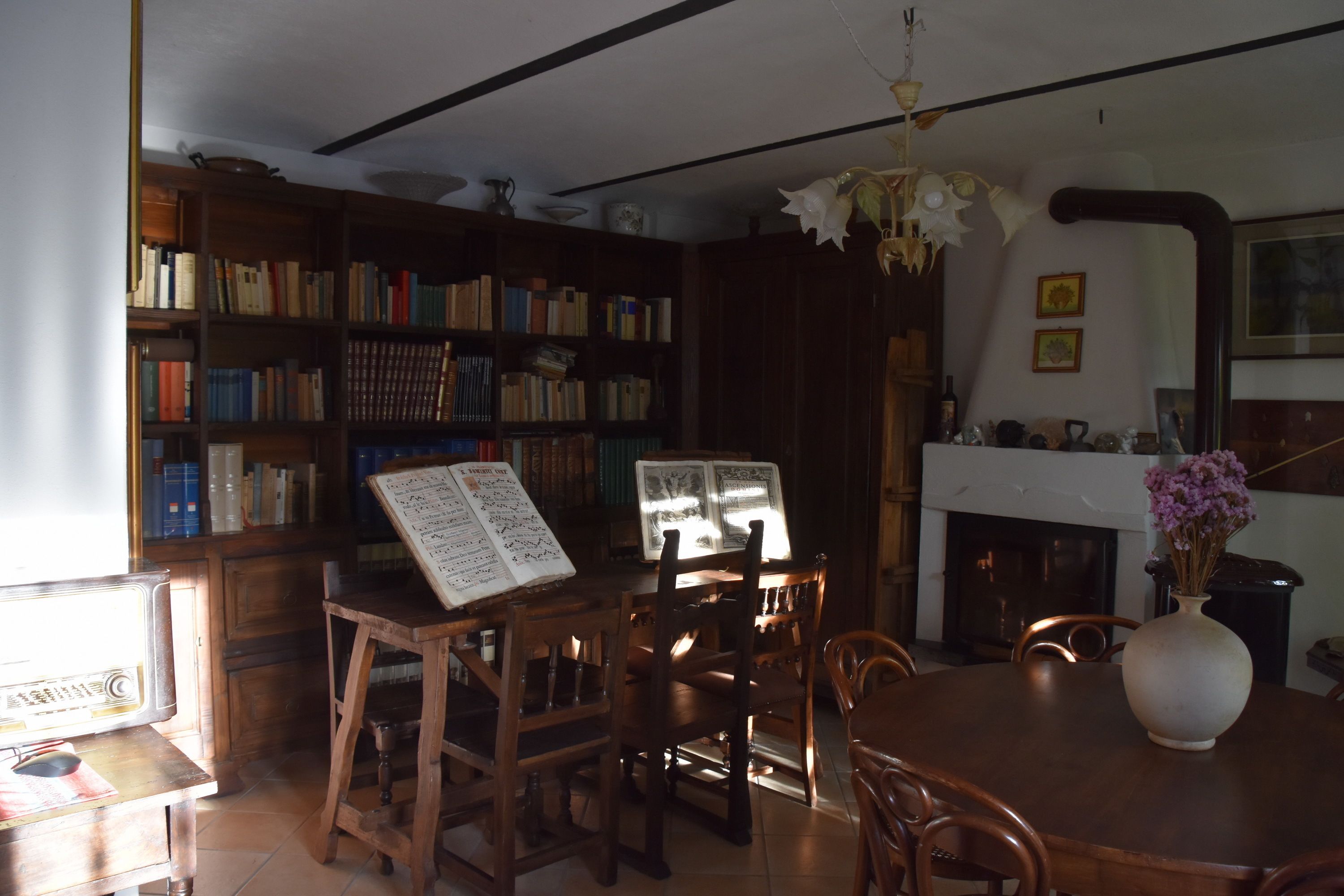 A library with bookshelves, a piano, a dining table, and a vase with flowers.