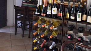 A wine cellar with multiple wine racks filled with bottles, a wooden chair, and a painting on the wall. - Agriturismo corte di Gerardo (Tonco)