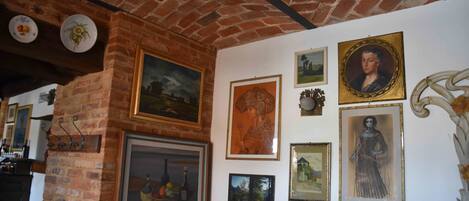 Habitación con pared de ladrillo y techo, decorada con diversas obras de arte enmarcadas y placas decorativas.