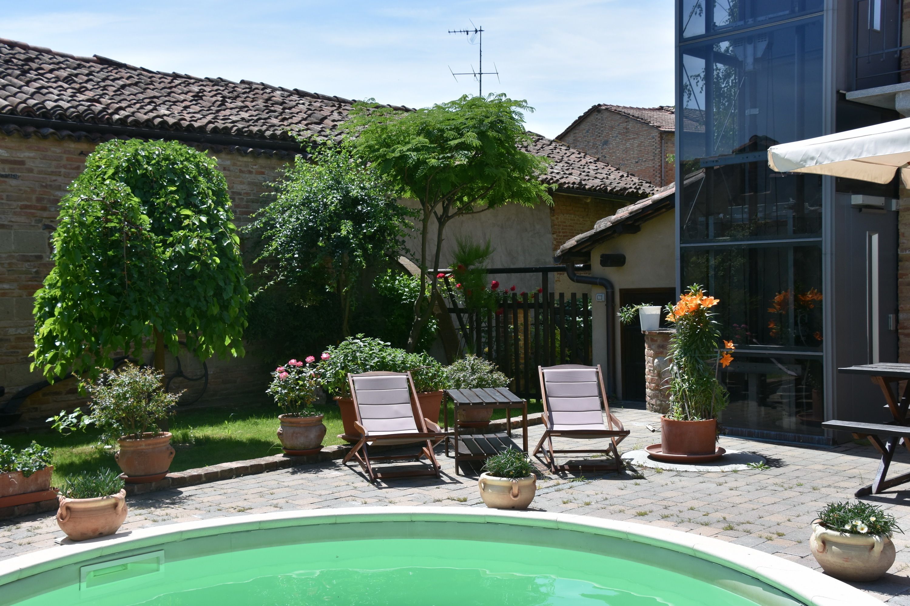 Un espace piscine avec des chaises longues, des plantes en pot et un bâtiment en briques en arrière-plan.