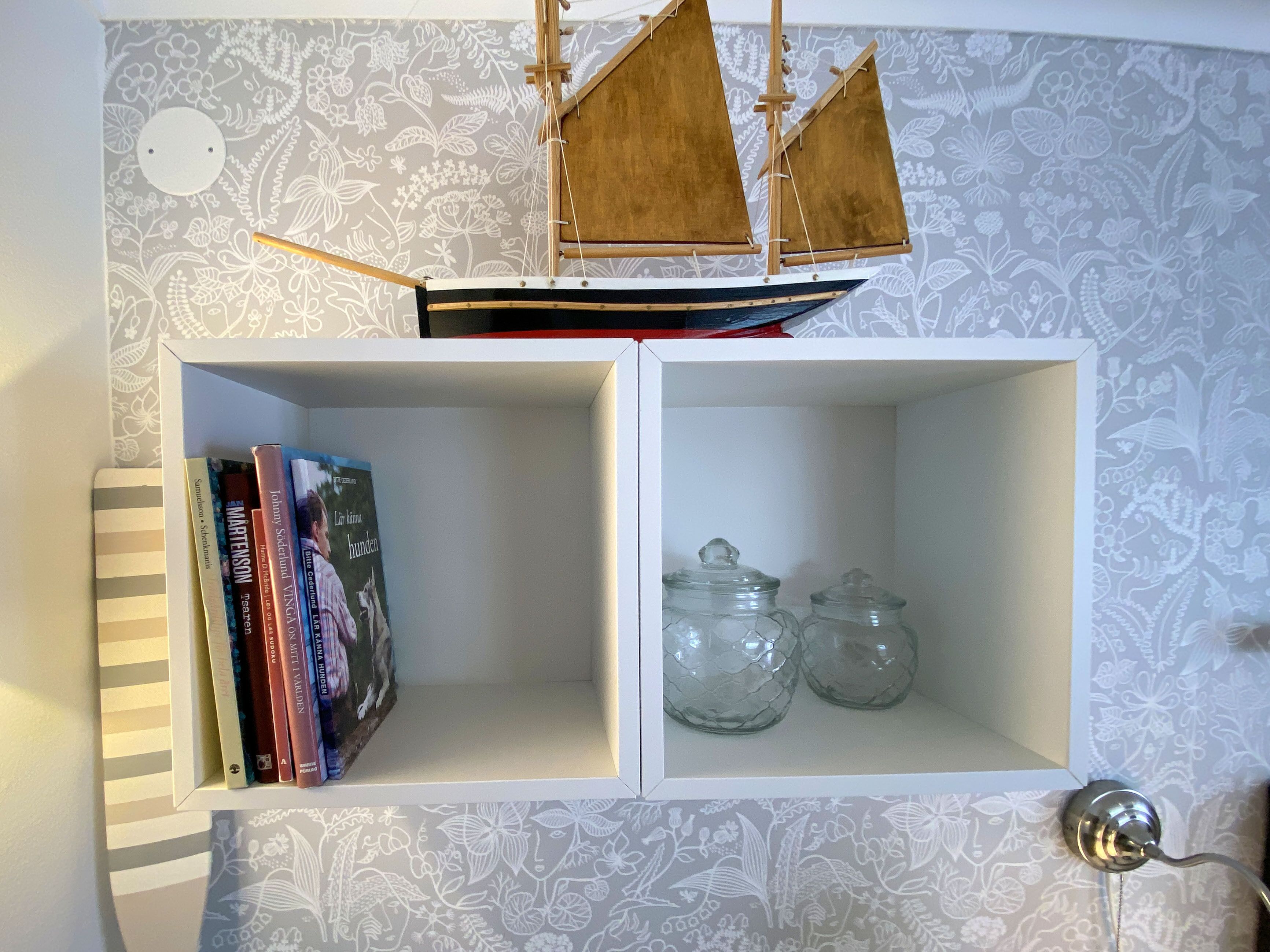 A bookshelf with books and two glass jars.