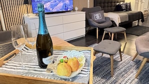 A modern hotel room with a television displaying a scenic view, a minibar, a sofa, and a dining area with a bottle of wine and snacks. - Skaftö Hotell Villa Lönndal, Grundsund (Grundsund)