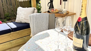 A cozy outdoor seating area with a wooden bench, a patterned tablecloth, and a bottle of champagne. - Skaftö Hotell Villa Lönndal, Grundsund (Grundsund)