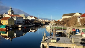 A calm waterway with boats docked, a wooden pier, and houses with distinct architectural styles. - Skaftö Hotell Villa Lönndal, Grundsund (Grundsund)