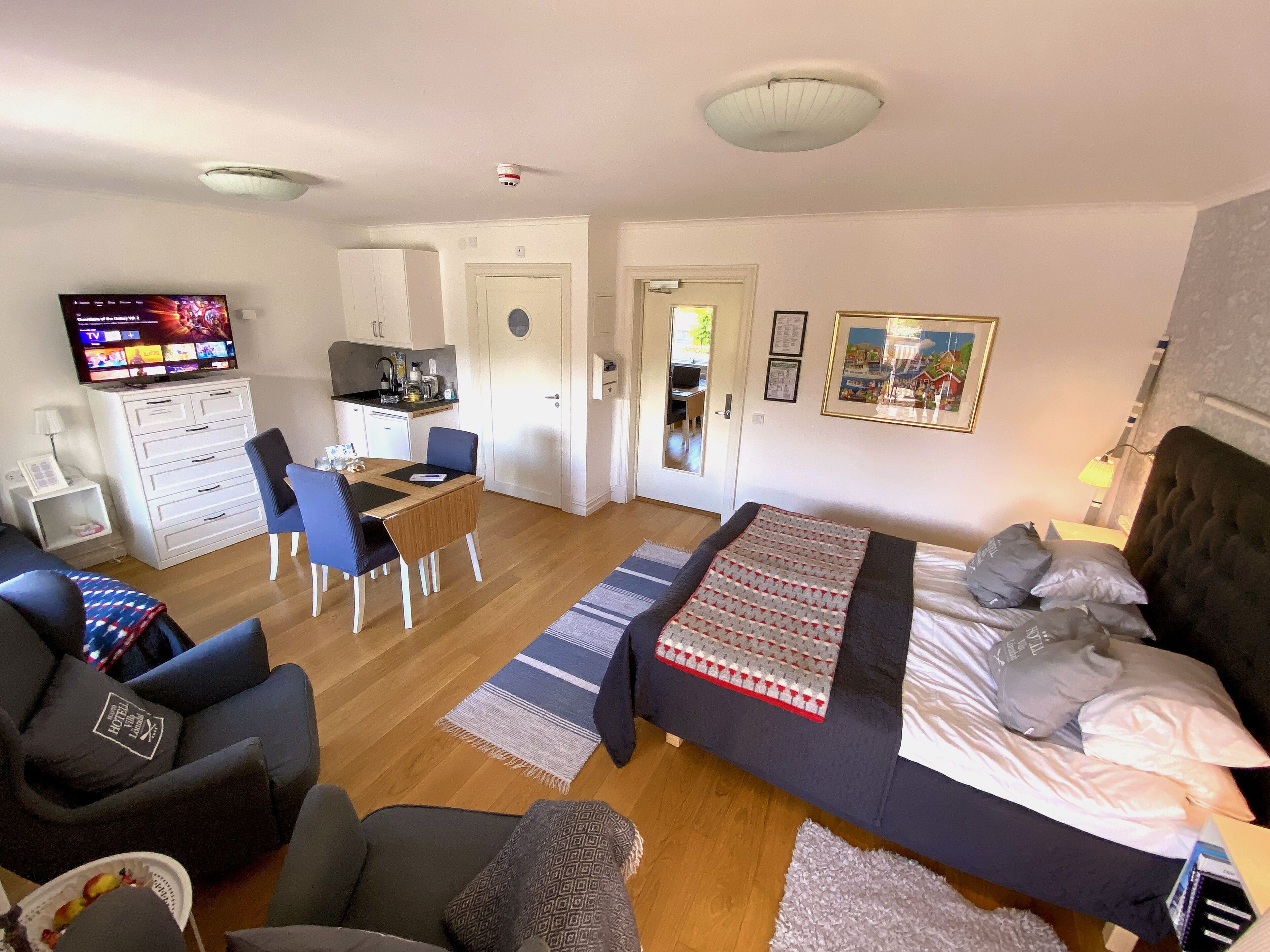 Ett hotellrum med en säng, ett skrivbord, en stol, en TV och ett litet kök.