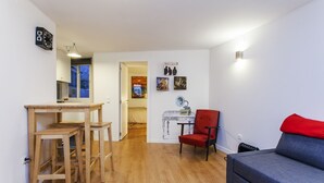 A living room with a sofa, a red chair, and a wooden table with chairs. There is a wall with framed pictures and a clock. - LxWay Apartments Praça da Alegria (Lisbon)