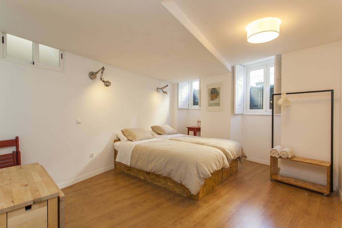 Une chambre avec un lit en bois, une petite table en bois et un miroir accroché au mur.