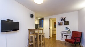 A compact living space with a flat-screen TV mounted on the wall, a wooden dining table with stools, a red chair, and a kitchen area visible through an open door. - LxWay Apartments Praça da Alegria (Lisbon)