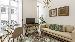 Un salon moderne avec une table à manger en verre, un canapé, un téléviseur posé sur un meuble en bois et des carreaux de sol à motifs.