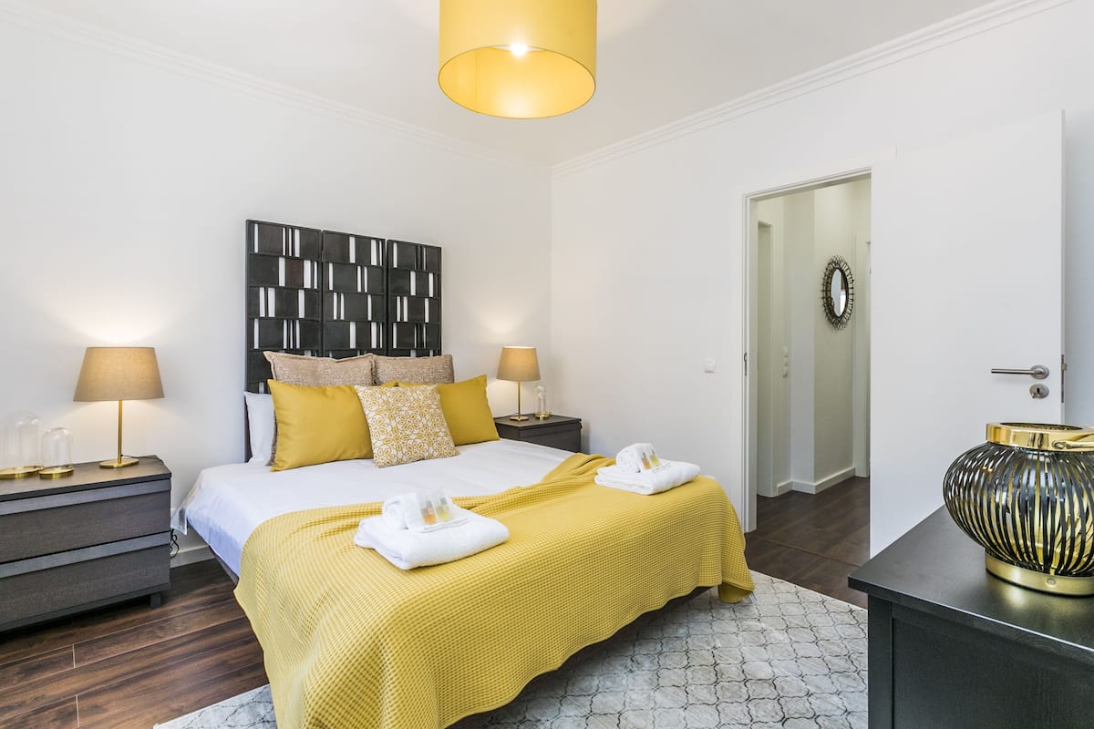 Ein Hotelzimmer mit Bett, zwei Nachttischen, einer Lampe, einer Wanddekoration und einer Tür mit Spiegel.