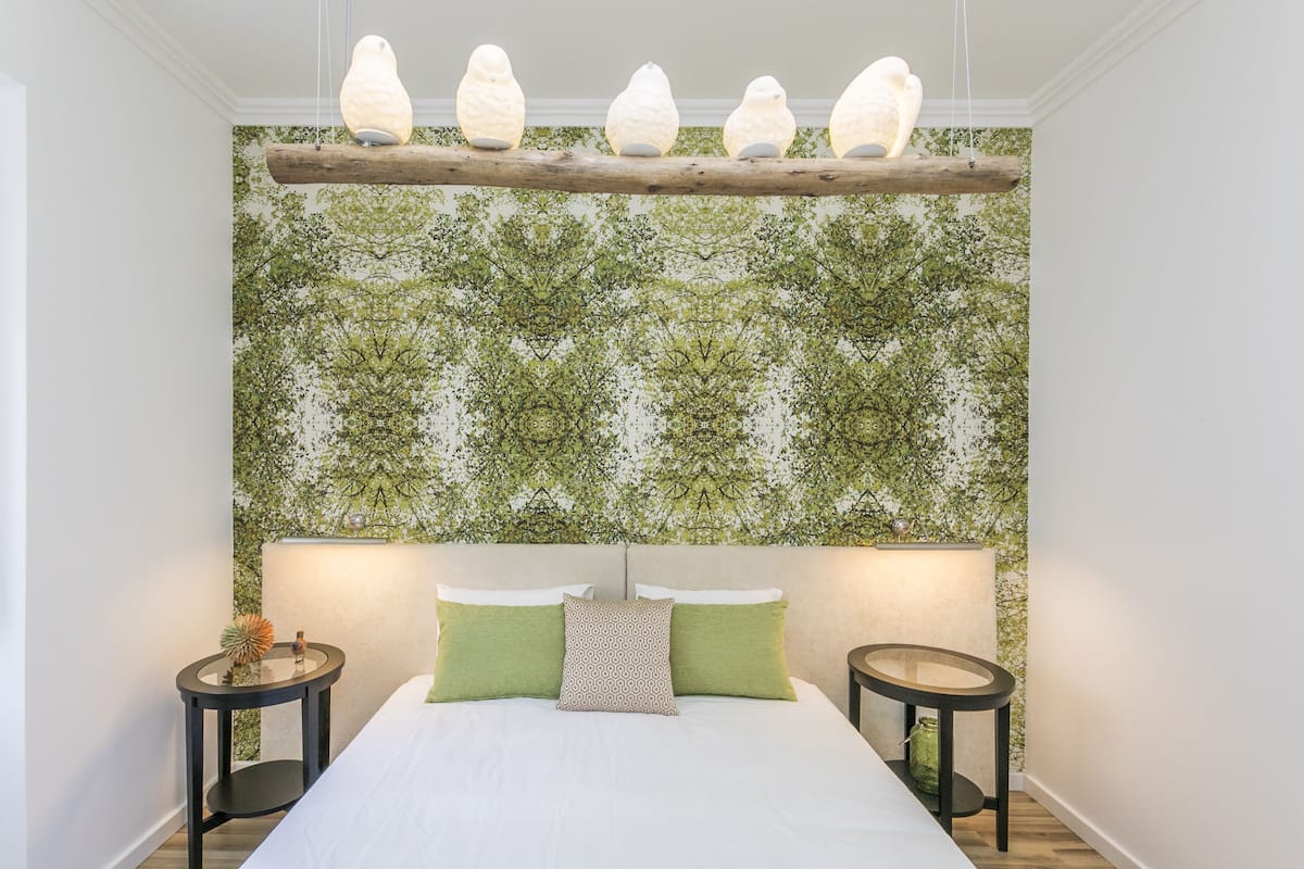 Ein Schlafzimmer mit einem Bett, zwei Nachttischen, einer Wandleuchte und einer Wand mit einem Blättermuster.