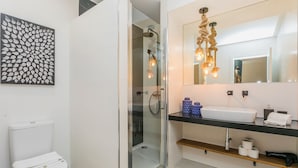 Een moderne badkamer met een glazen douchecabine, een wit toilet, een wastafel met een zwart aanrechtblad en een spiegel met een decoratieve verlichtingsarmatuur.