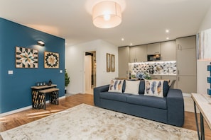 Ein modernes Wohnzimmer mit blauer Akzentwand, einem grauen Sofa mit Zierkissen, einem Holztisch und einem großen Teppich.