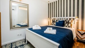 Een hotelkamer met een grote spiegel, een bed met blauw beddengoed, een gestreepte wand en een nachtkastje met een lamp.