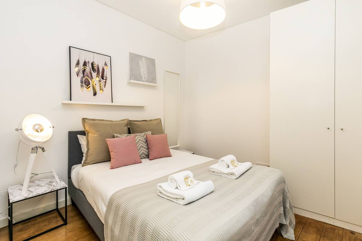 A neatly arranged bedroom with a bed, pillows, a bedside lamp, and a wardrobe.