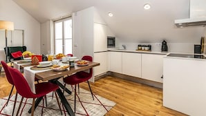 A modern kitchen with white cabinets, a wooden dining table, red chairs, and a small island with a sink. - LxWay Apartments Galeria Alfama (Lisbon)