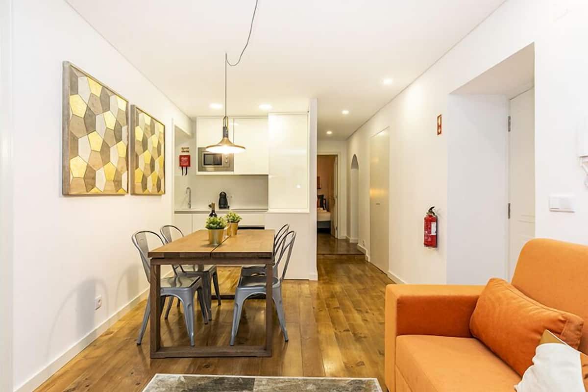 A compact living space with a dining area, a sofa, and a kitchen in the background.