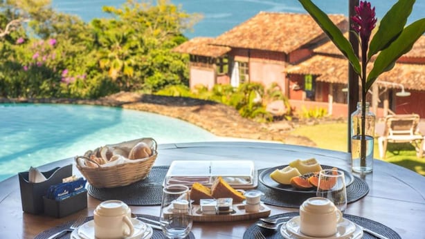 Une table dressée avec des aliments pour le petit-déjeuner, une vue sur l’océan et un paysage tropical.