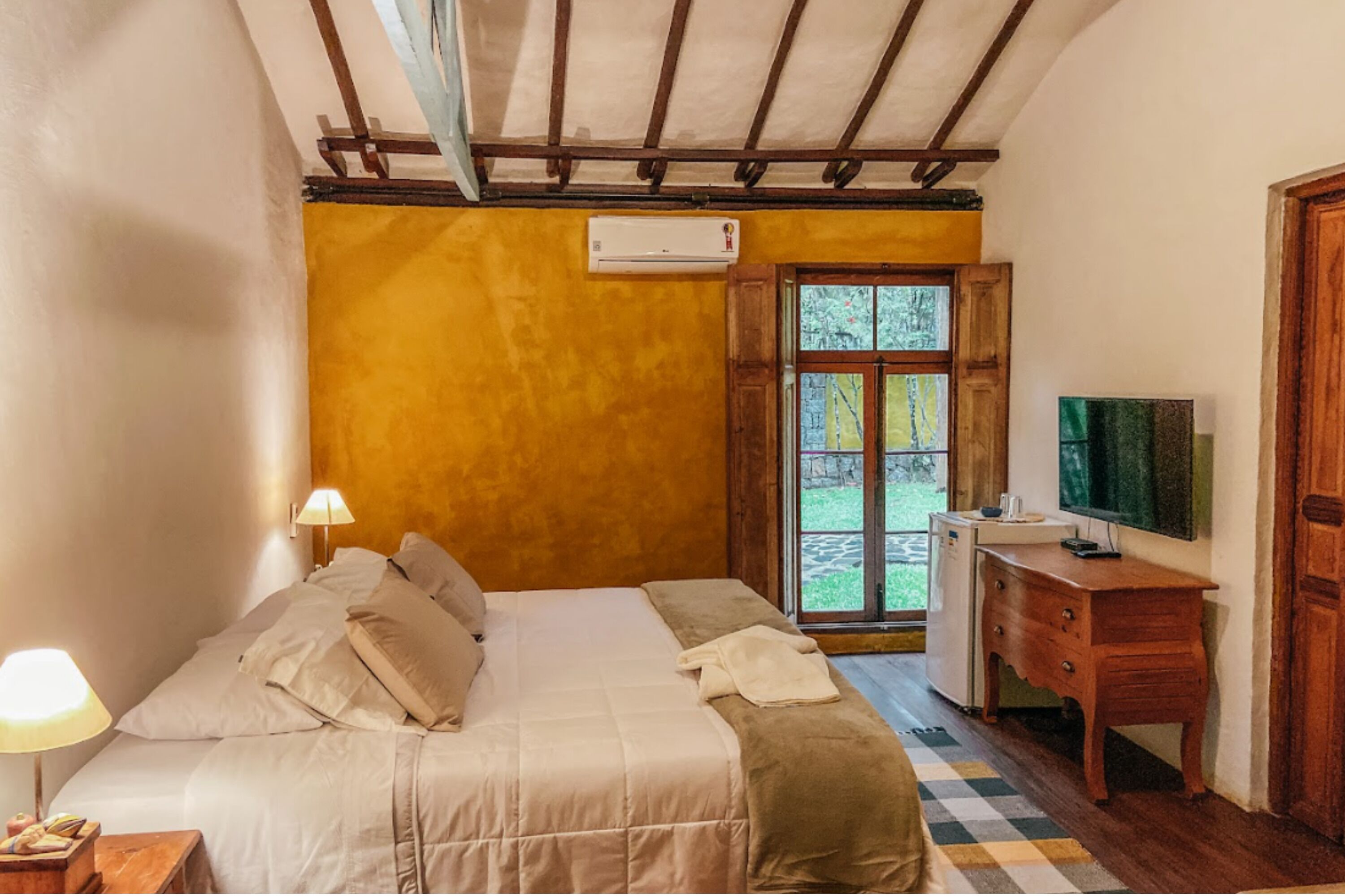 A bedroom with a bed, bedside lamps, a dresser, a television, and a window with a view.