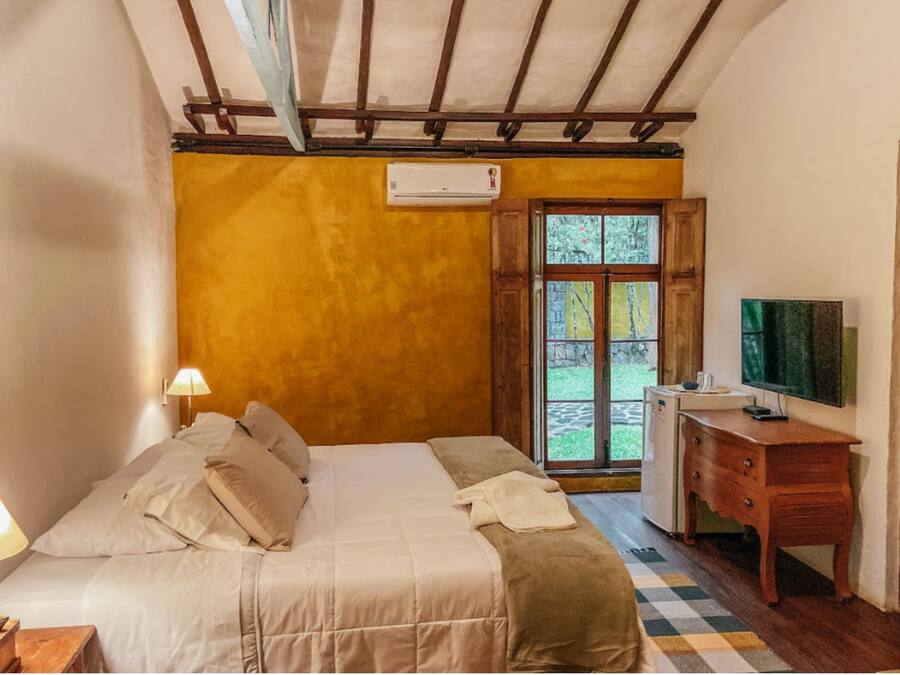 A bedroom with a bed, bedside lamps, a dresser, a television, and a window with a view.