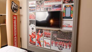 A room with a large flat-screen TV mounted on a wall, surrounded by framed sports memorabilia and a wooden cabinet with a bear logo.