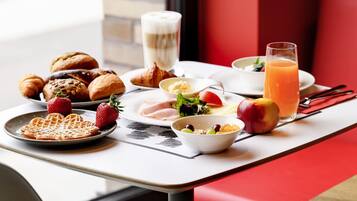 A breakfast setting with croissants, waffles, a strawberry, a glass of orange juice, and a bowl of salad on a table.