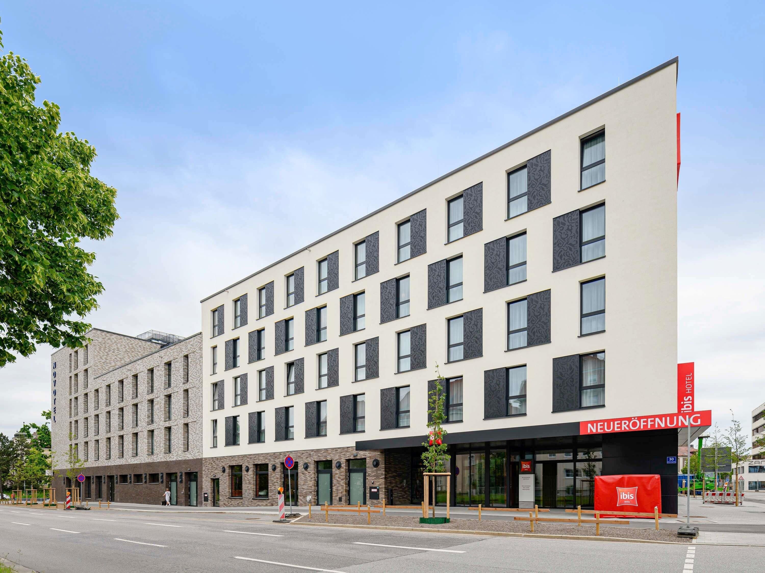 Un hotel moderno con fachada plana, múltiples ventanas y un cartel que indica una nueva apertura.