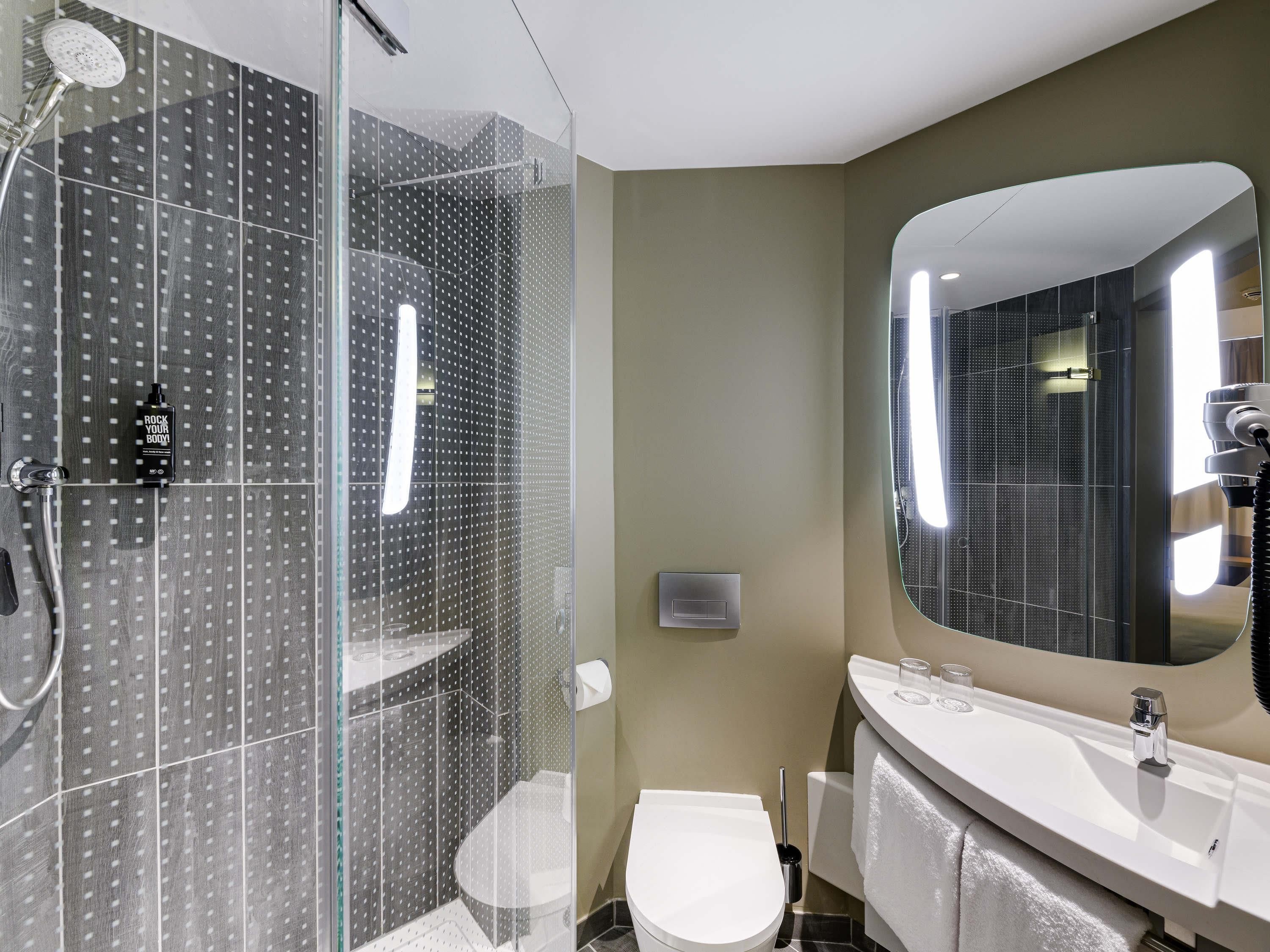 A modern bathroom with a glass-enclosed shower, a large mirror, and a white sink.