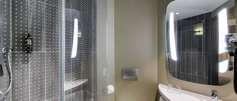 A modern bathroom with a glass-enclosed shower, a large mirror, and a white sink.