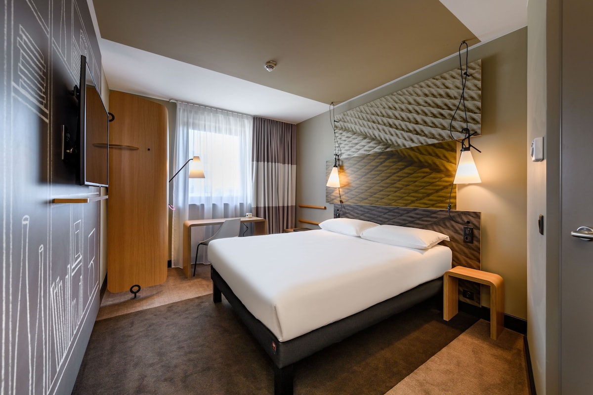 Une chambre d’hôtel moderne avec un grand lit, un bureau, une télévision et un mur décoré d’un motif.