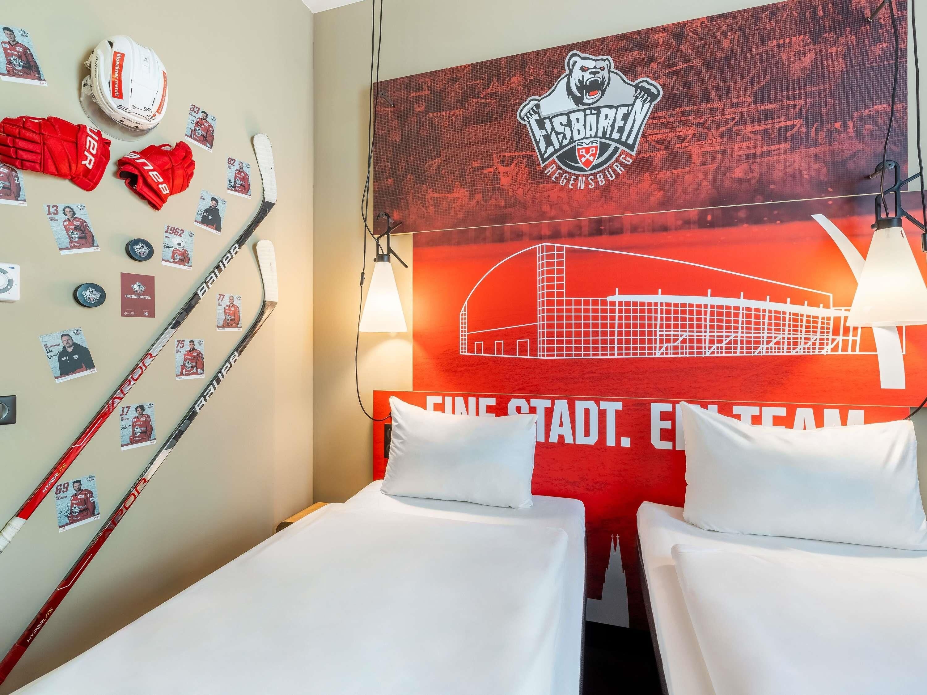 A hotel room with two beds, a hockey helmet, gloves, and hockey cards on the wall.