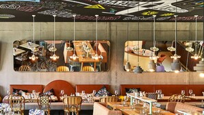 Um restaurante com várias áreas de refeição, incluindo cabines e mesas, com luminárias pendentes e um carpete estampado.