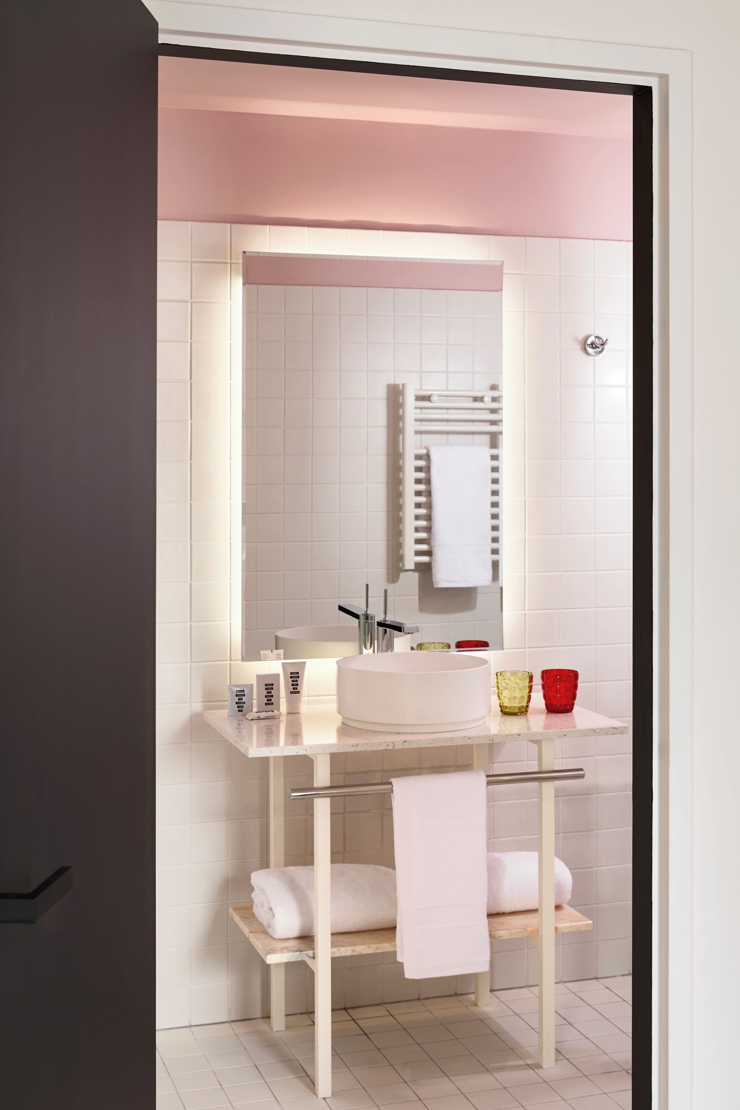 A modern bathroom with a white sink, mirror, and towel rack. There are two towels hanging on the rack.