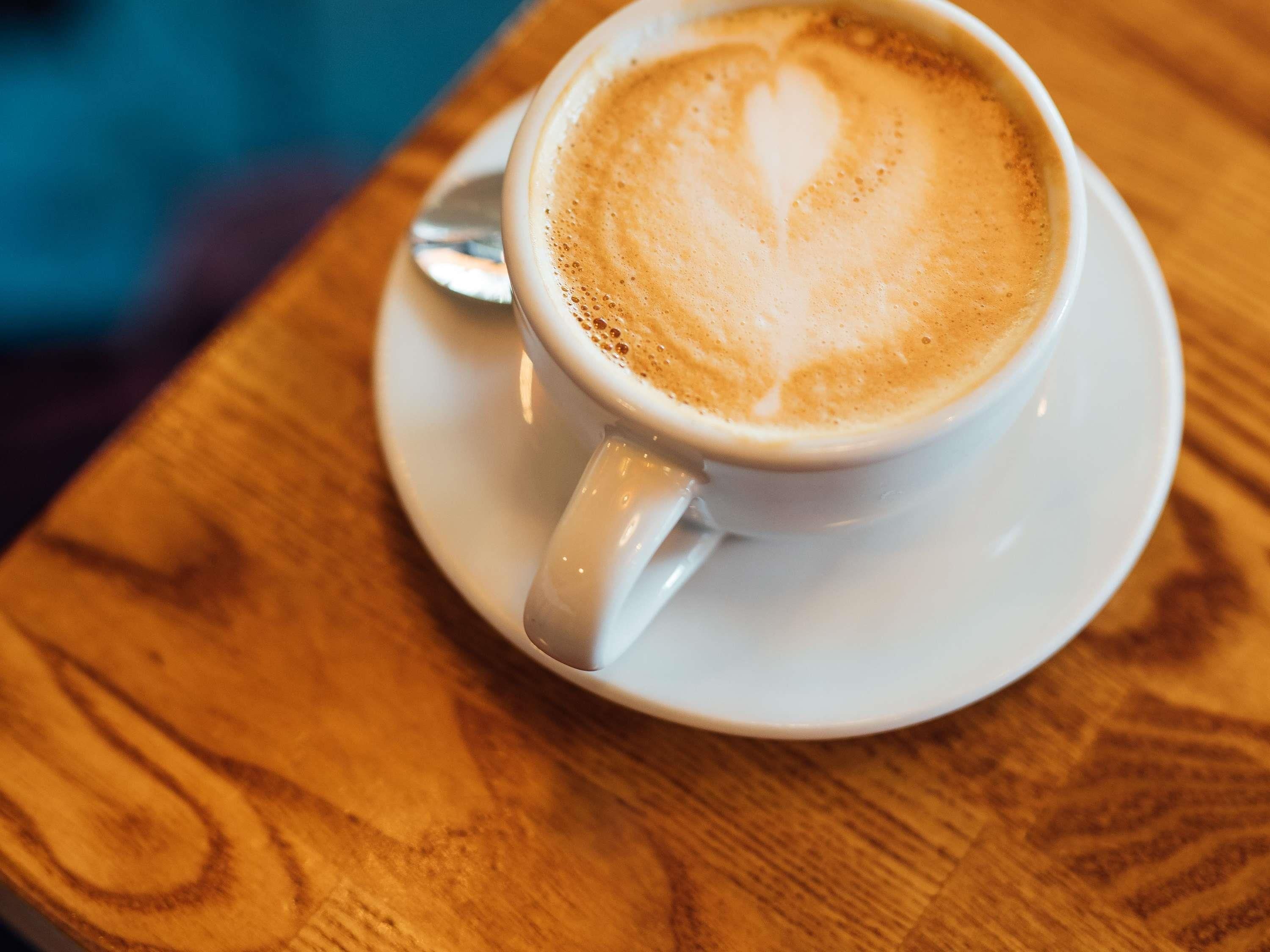 Une tasse de café sur une soucoupe, avec un motif en forme de cœur réalisé avec de la mousse de lait, posée sur une table en bois.