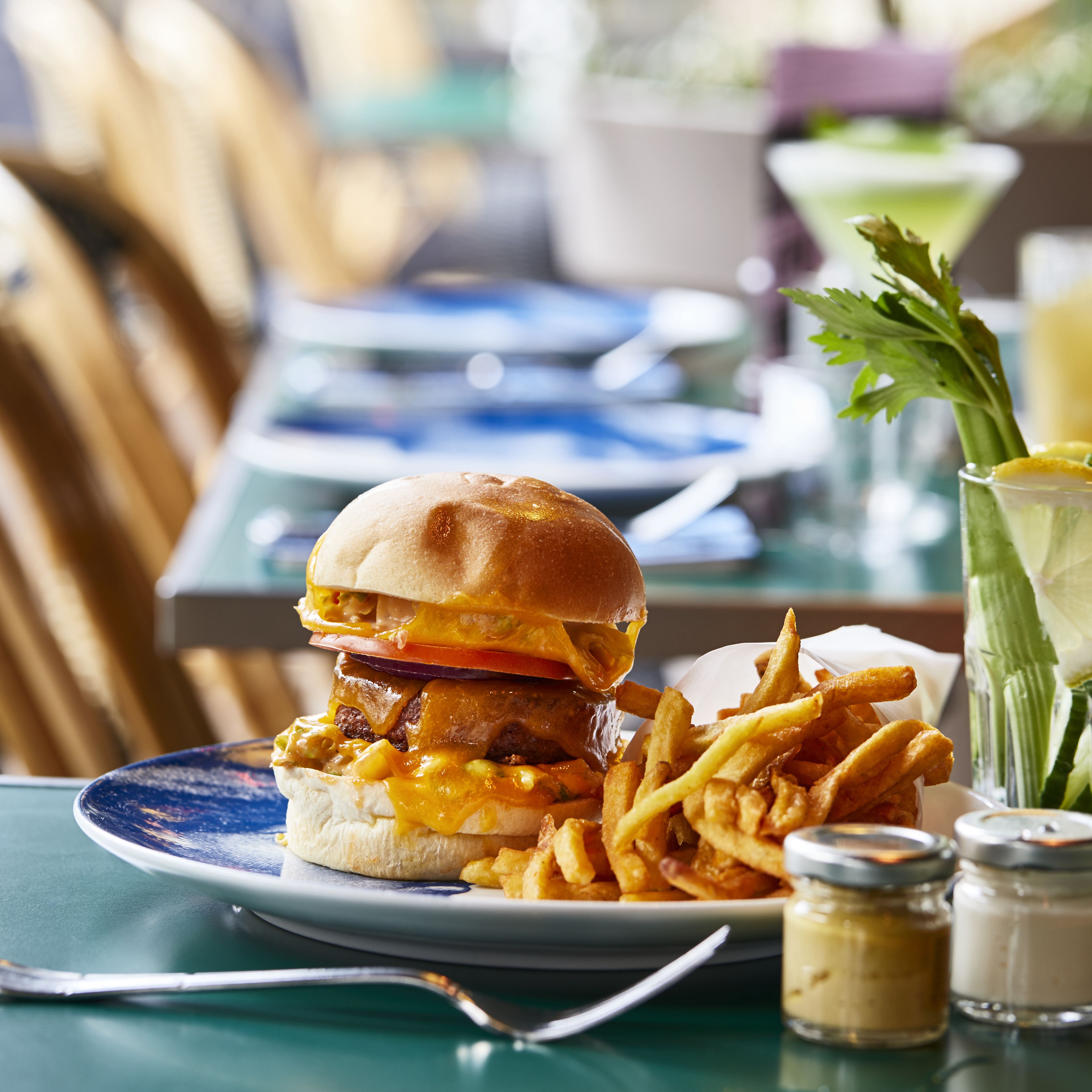 Een maaltijd bestaande uit een hamburger, friet en een drankje op een tafel.
