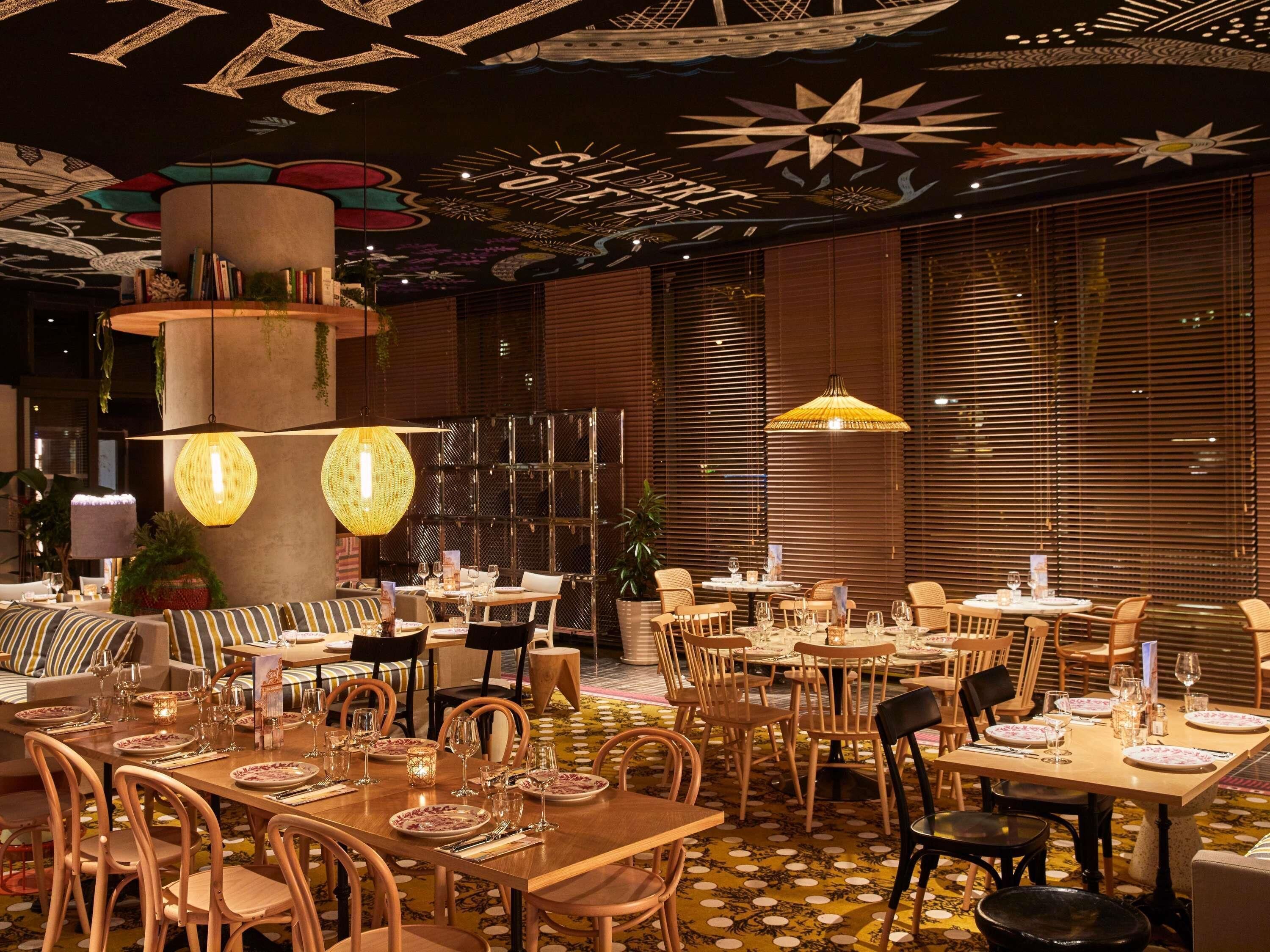 A restaurant with multiple dining tables, chairs, and hanging lamps.
