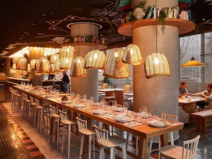 A restaurant with long communal tables, hanging wicker lamps, and a modern interior design. - Mama Shelter Paris West (Paris)