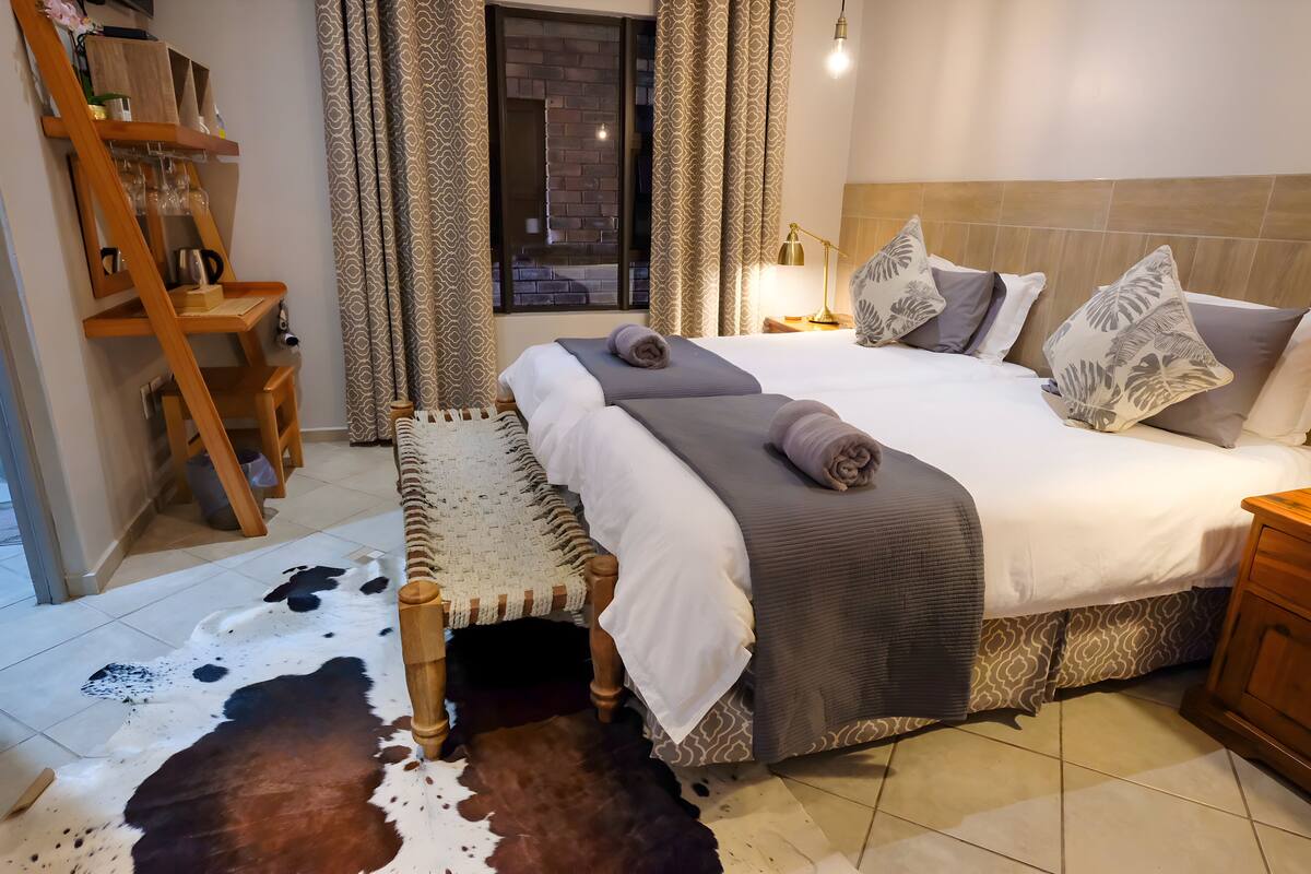 Quarto com uma cama grande, uma escada de madeira, um tapete de couro de vaca e vista para o exterior através de uma janela.