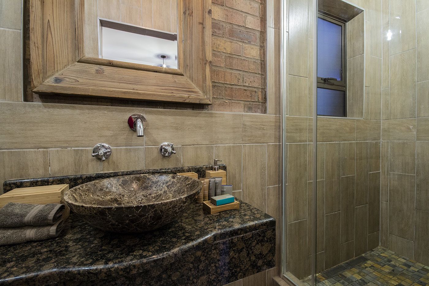 A bathroom with a granite sink, wooden vanity, and a glass shower enclosure.